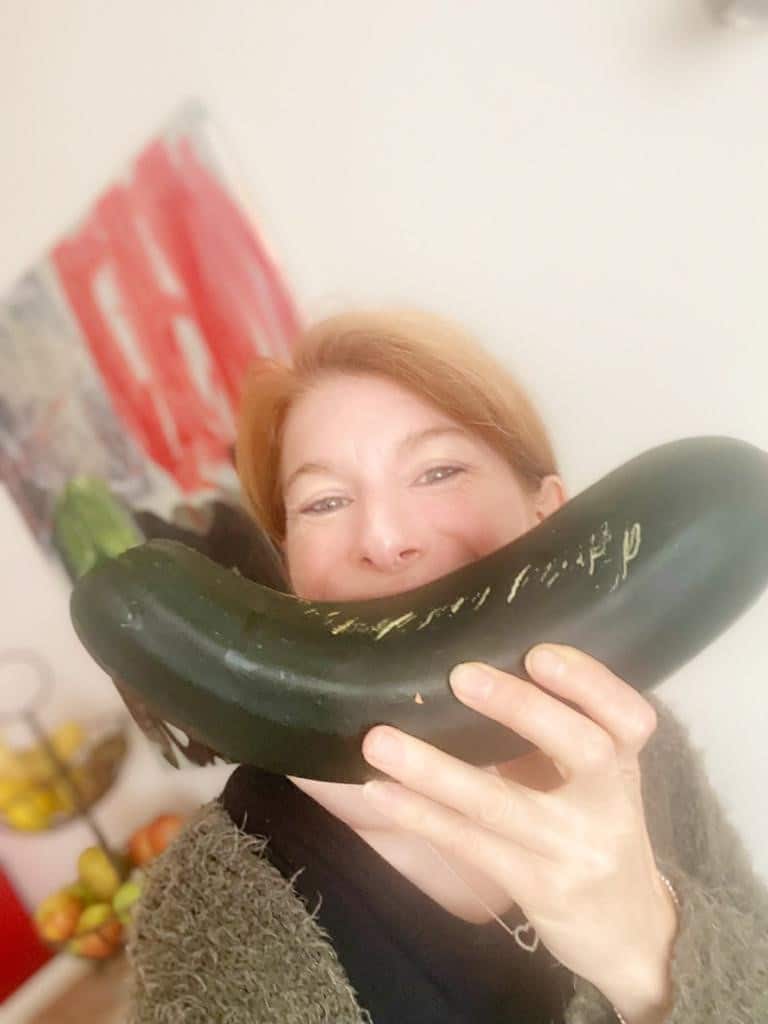 Darmkrebs-Patientin hält eine gesunde Zucchini wie einen Lächelnden Mund vor ihr Gesicht