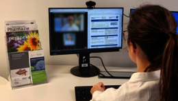 Wissenschaftlerin sitzt am PC in einer Online-Konferenz und schaut auf ein Arzneimittelmerkblatt. Daneben stehen Prospekte wie zum Thema "Beratung bei oraler Tumortherapie"