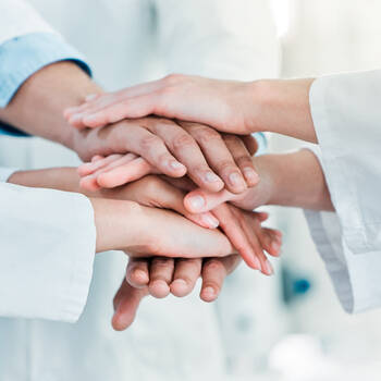 Nahaufnahme einer Gruppe nicht erkennbarer Wissenschaftler, die ihre Hände in einem Huddle in einem Labor zusammenfügen, um eine Allianz zu bilden
