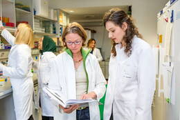 Die junge Ärztin Dr. Laura Hinze steht im Labor und bespricht Notizen mit einer Frau im weißen Kittel